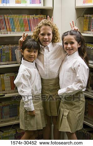 Portrait of schoolgirls showing victory sign over each other's head in the library View Large Photo Image Stock Image - Portrait of schoolgirls showing victory sign over each other's head in the library. Fotosearch