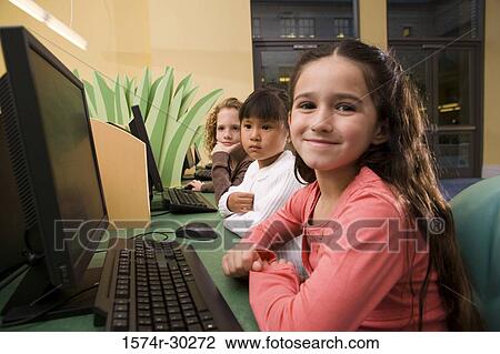 Stock Image - Portrait of schoolgirls sitting by computer in the library. Fotosearch