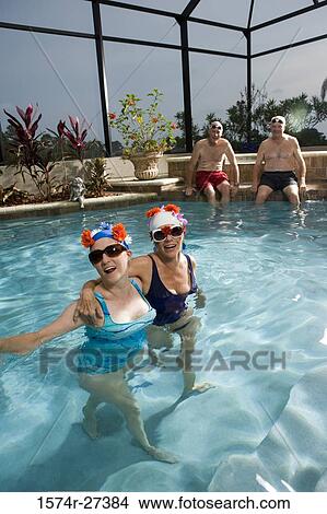 Picture - Portrait of senior women outside swimming pool while senior men sitting in background. Fotosearch