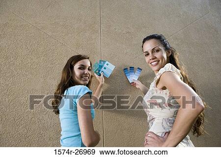 Stock Photo - Portrait of sisters holding color swatches against wall. Fotosearch