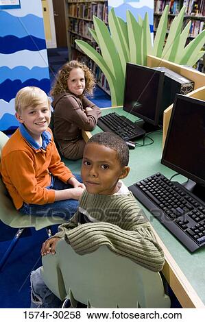 Stock Photo - Portrait of smiling schoolboys and a girl sitting with computers in the library. Fotosearch