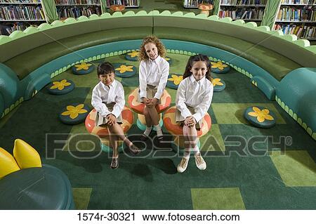 Portrait of smiling schoolgirls sitting on stool in the library View Large Photo Image Stock Image - Portrait of smiling schoolgirls sitting on stool in the library. Fotosearch