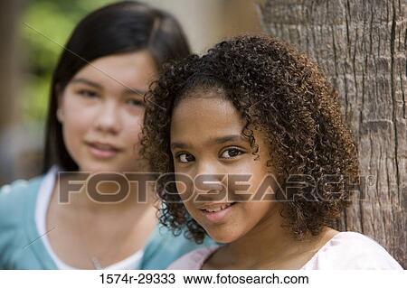 Portrait of teenage girls standing by a tree trunk View Large Photo Image Stock Image - Portrait of teenage girls standing by a tree trunk. Fotosearch