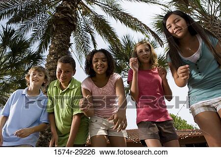Stock Photograph - Portrait of teenagers dancing under a palm tree. Fotosearch