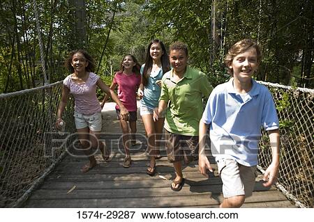 Portrait of teenagers running on a rope bridge with trees in the background View Large Photo Image Stock Photo - Portrait of teenagers running on a rope bridge with trees in the background. Fotosearch