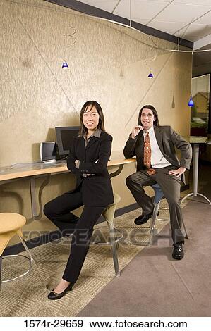 Portrait of young businessmen and businesswoman sitting by desk in an office View Large Photo Image Stock Photo - Portrait of young businessmen and businesswoman sitting by desk in an office. Fotosearch