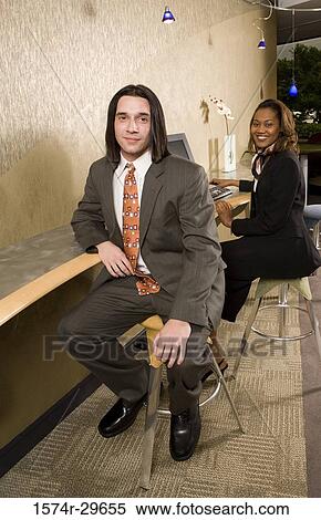 Portrait of young businessmen and businesswoman sitting by desk in an office View Large Photo Image Stock Photography - Portrait of young businessmen and businesswoman sitting by desk in an office. Fotosearch