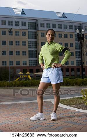 Portrait of young woman in sports clothing standing on walkway with building in the background View Large Photo Image Stock Image - Portrait of young woman in sports clothing standing on walkway with building in the background. Fotosearch