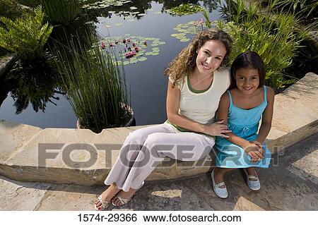 Portrait of young woman with her daughter sitting by pond View Large Photo Image Stock Photograph - Portrait of young woman with her daughter sitting by pond. Fotosearch