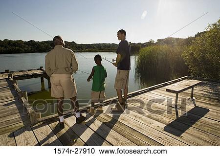 Stock Image - Rear view of a man fishing with his son and friend on jetty. Fotosearch