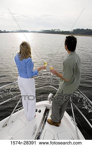 Rear view of a mid adult couple standing with glass of champagne at bow of a boat View Large Photo Image Stock Image - Rear view of a mid adult couple standing with glass of champagne at bow of a boat. Fotosearch