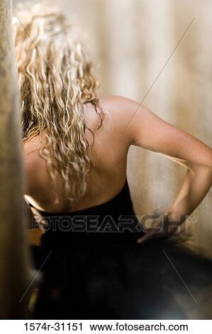 Stock Image - Rear view of young woman standing with hand on hip. Fotosearch