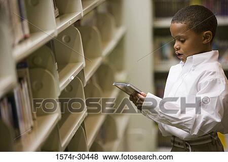 Stock Photo - Schoolboy holding a compact disk in the library. Fotosearch