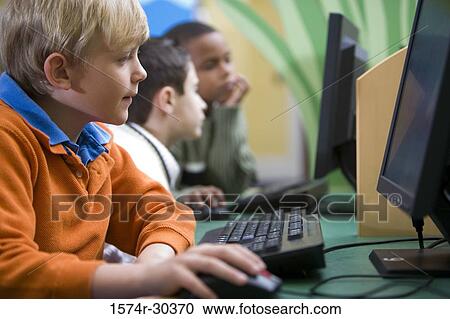 Stock Image - Schoolboy using computer in the library. Fotosearch