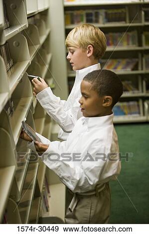 Stock Photo - Schoolboys looking at compact discs in front of shelf in the library. Fotosearch