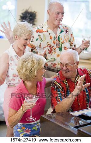 Stock Photo - Senior man playing piano while friends listening the music. Fotosearch