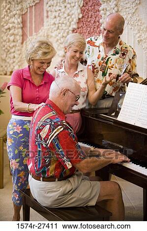 Stock Image - Senior men playing piano while friends listening the music. Fotosearch