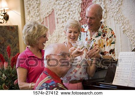 Stock Image - Senior men playing piano while friends listening the music. Fotosearch