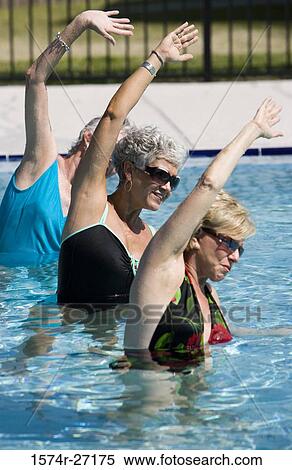 Stock Photography - Senior women exercising with arms raised in swimming pool. Fotosearch