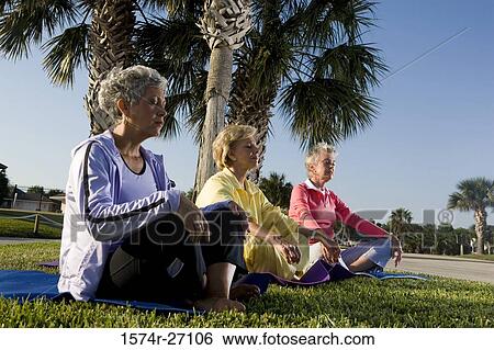 Stock Photograph - Senior women sitting on exercise mat and meditating. Fotosearch