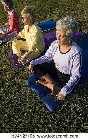 Stock Photography - Senior women sitting on exercise mat and meditating. Fotosearch