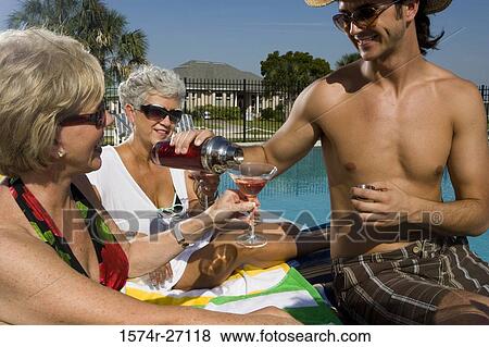 Shirtless young man serving drink to senior woman by pool View Large Photo Image Stock Photo - Shirtless young man serving drink to senior woman by pool. Fotosearch