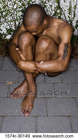 Stock Photo - Shirtless young man sitting on floor and hugging his knees. Fotosearch