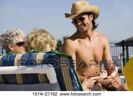 Stock Image - Shirtless young man sitting with senior women. Fotosearch