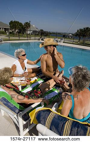 Shirtless young man sitting with senior women by pool View Large Photo Image Stock Photo - Shirtless young man sitting with senior women by pool. Fotosearch
