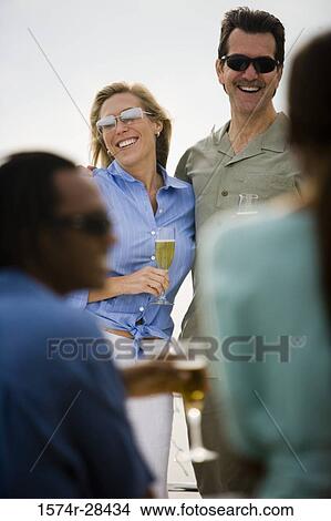 Smiling mid adult couple standing with glass of champagne View Large Photo Image Picture - Smiling mid adult couple standing with glass of champagne. Fotosearch