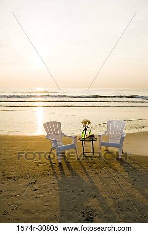 Stock Photography - Table with chairs arranged on the beach with sunset in background. Fotosearch