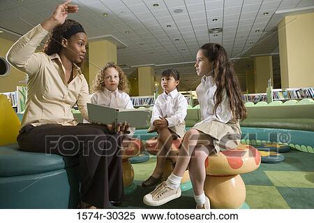 Teacher holding a book and gesturing to schoolgirls in the library View Large Photo Image Stock Photography - Teacher holding a book and gesturing to schoolgirls in the library. Fotosearch