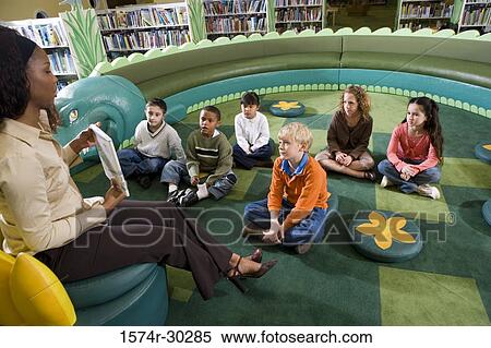 Teacher holding book while students sitting on floor in the library View Large Photo Image Stock Photography - Teacher holding book while students sitting on floor in the library. Fotosearch