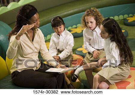 Teacher looking at a book and gesturing to schoolgirls in the library View Large Photo Image Stock Image - Teacher looking at a book and gesturing to schoolgirls in the library. Fotosearch