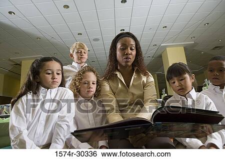 Teacher reading out to students in the library View Large Photo Image Stock Photograph - Teacher reading out to students in the library. Fotosearch