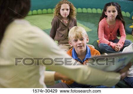 Stock Photo - Teacher showing book to students in the library. Fotosearch