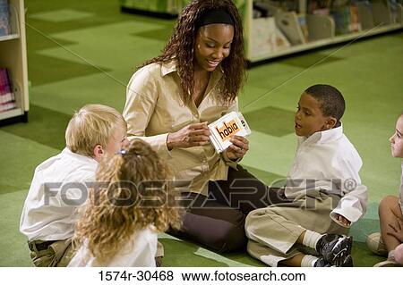 Stock Photo - Teacher showing flash cards to students sitting on floor in the library. Fotosearch