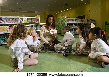 Stock Photograph - Teacher showing flash cards to students sitting on floor in the library. Fotosearch