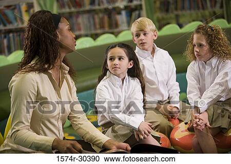 Teacher sitting with students in the library View Large Photo Image Stock Image - Teacher sitting with students in the library. Fotosearch