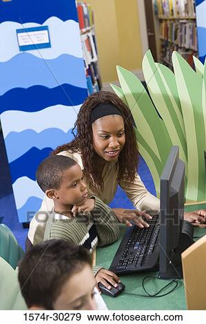 Teacher teaching schoolboy computer in the library View Large Photo Image Stock Photo - Teacher teaching schoolboy computer in the library. Fotosearch