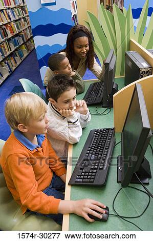 Teacher teaching schoolboys computer in the library View Large Photo Image Stock Photo - Teacher teaching schoolboys computer in the library. Fotosearch