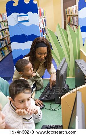Stock Photo - Teacher teaching schoolboys computer in the library. Fotosearch