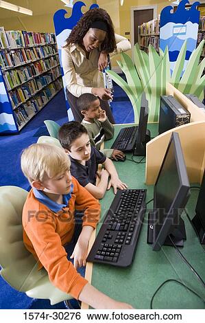 Teacher teaching schoolboys computer in the library View Large Photo Image Stock Photograph - Teacher teaching schoolboys computer in the library. Fotosearch