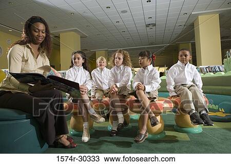 Teacher with a book sitting with students in the library View Large Photo Image Stock Image - Teacher with a book sitting with students in the library. Fotosearch