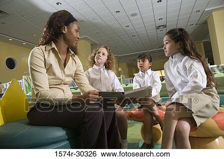 Stock Photograph - Teacher with a book sitting with schoolgirls in the library. Fotosearch