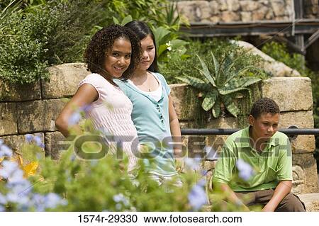 Teenage girls standing together with hand on hip and a boy sitting in the background View Large Photo Image Stock Image - Teenage girls standing together with hand on hip and a boy sitting in the background. Fotosearch
