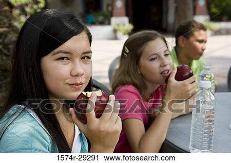 Teenagers sitting by a table and eating apples View Large Photo Image Stock Image - Teenagers sitting by a table and eating apples. Fotosearch