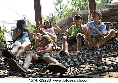 Stock Image - Teenagers sitting on net tied to wooden columns. Fotosearch