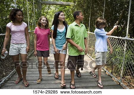 Teenagers walking on a rope bridge with trees in the background View Large Photo Image Stock Photography - Teenagers walking on a rope bridge with trees in the background. Fotosearch