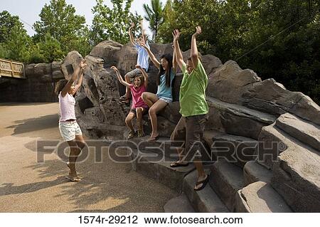 Stock Image - Teenagers with their arms raised sitting on rocks and playing. Fotosearch